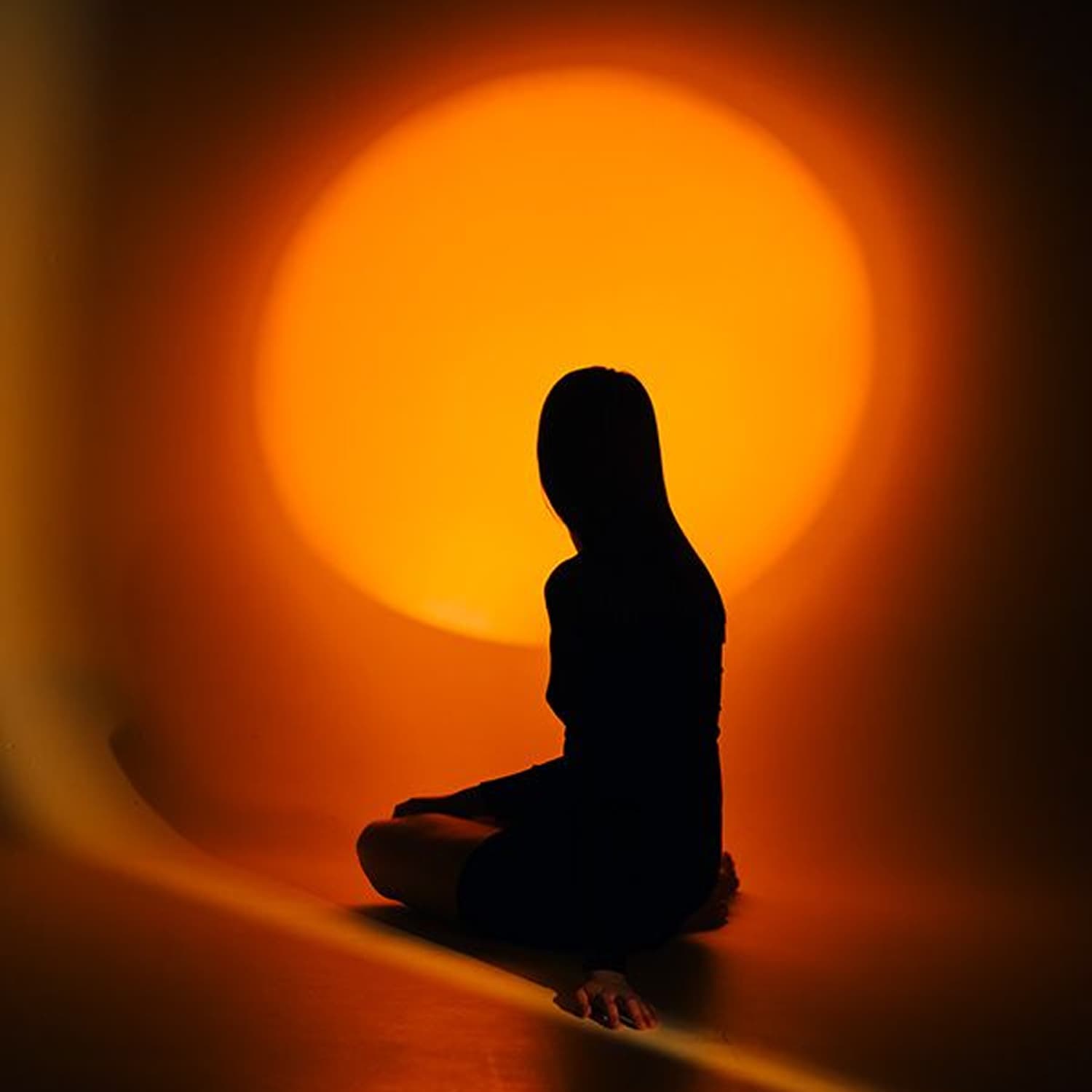 Silhouette di una persona seduta in meditazione davanti a una grande luce arancione e calda